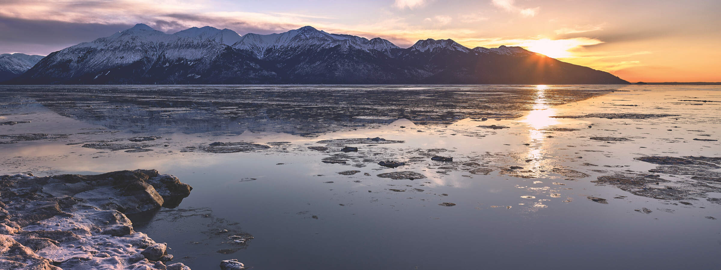 The sun peeks over the Kenai Mountains across Turnagain Arm near Anchorage